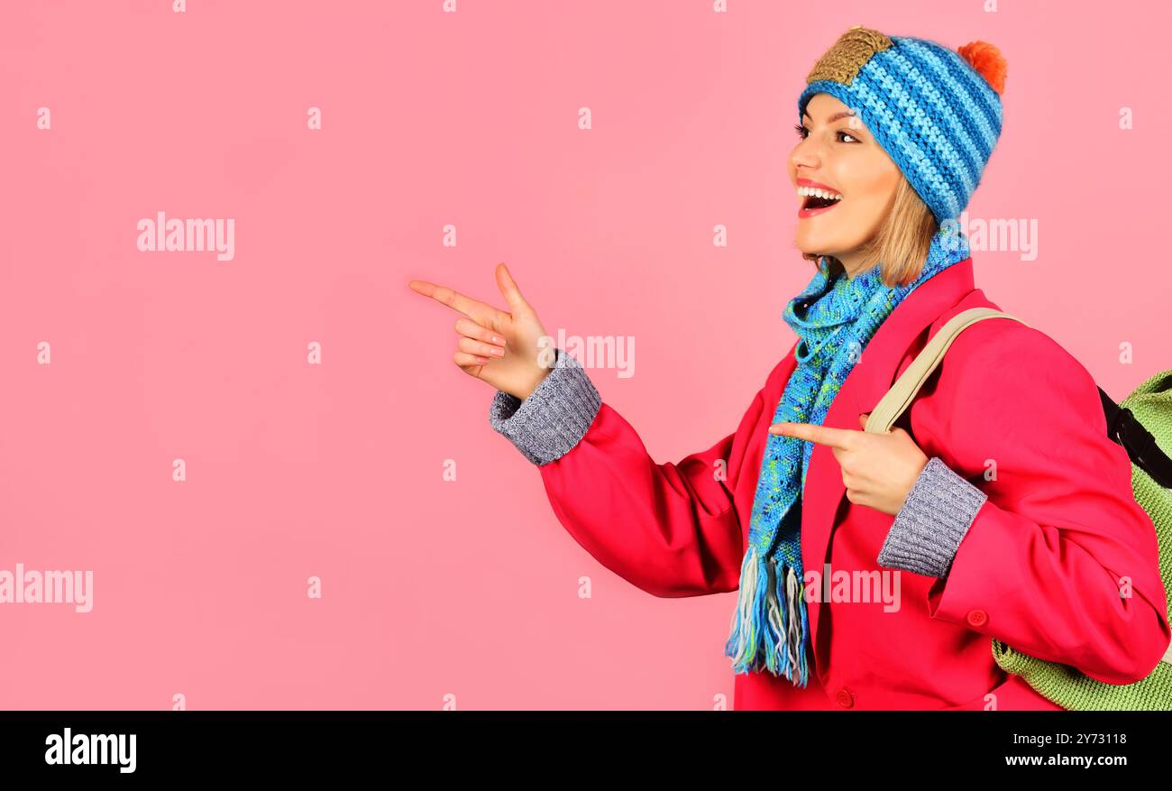 Donna sorridente con cappello blu, sciarpa e cappotto rosso con borsetta che punta le dita verso lo spazio di copia per la pubblicità. Sconti e sconti stagionali. Ragazza elegante in f Foto Stock