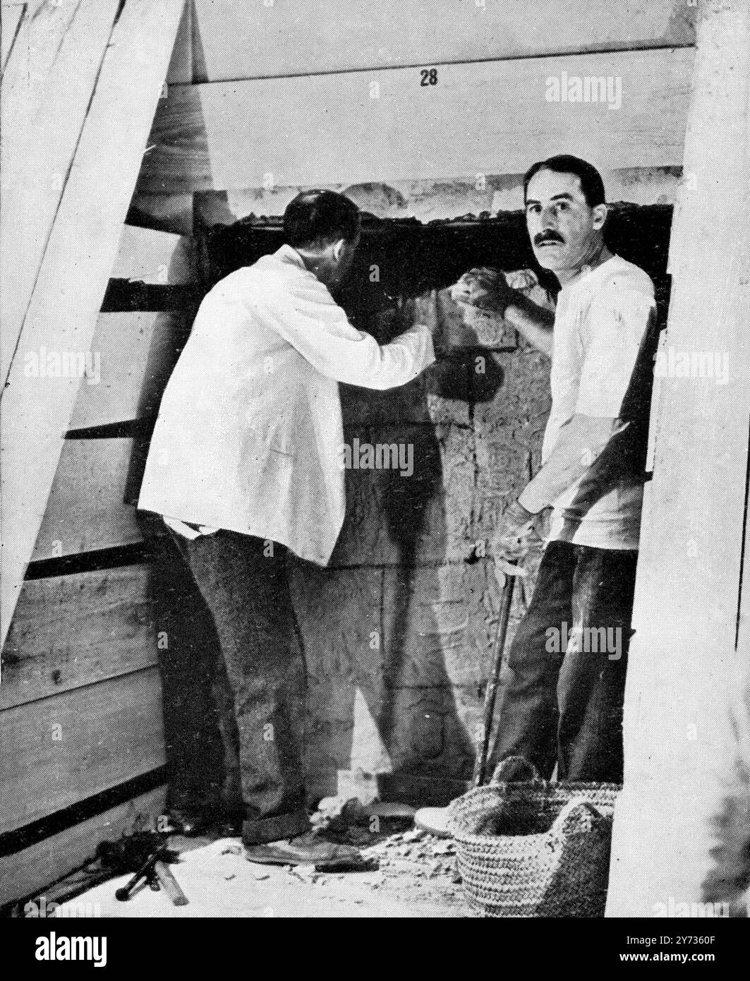 La prima tappa dell'apertura del sepolcro di Tutankhamon: Lord Carnavon (a sinistra) sbircia attraverso lo stretto buco finora realizzato da Howard Carter (a destra) 1923 Foto Stock