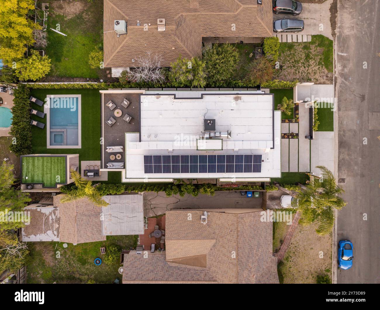 Vista aerea delle case suburbane con tetto a pannelli solari, piscina e prati verdi in un quartiere residenziale. Foto Stock