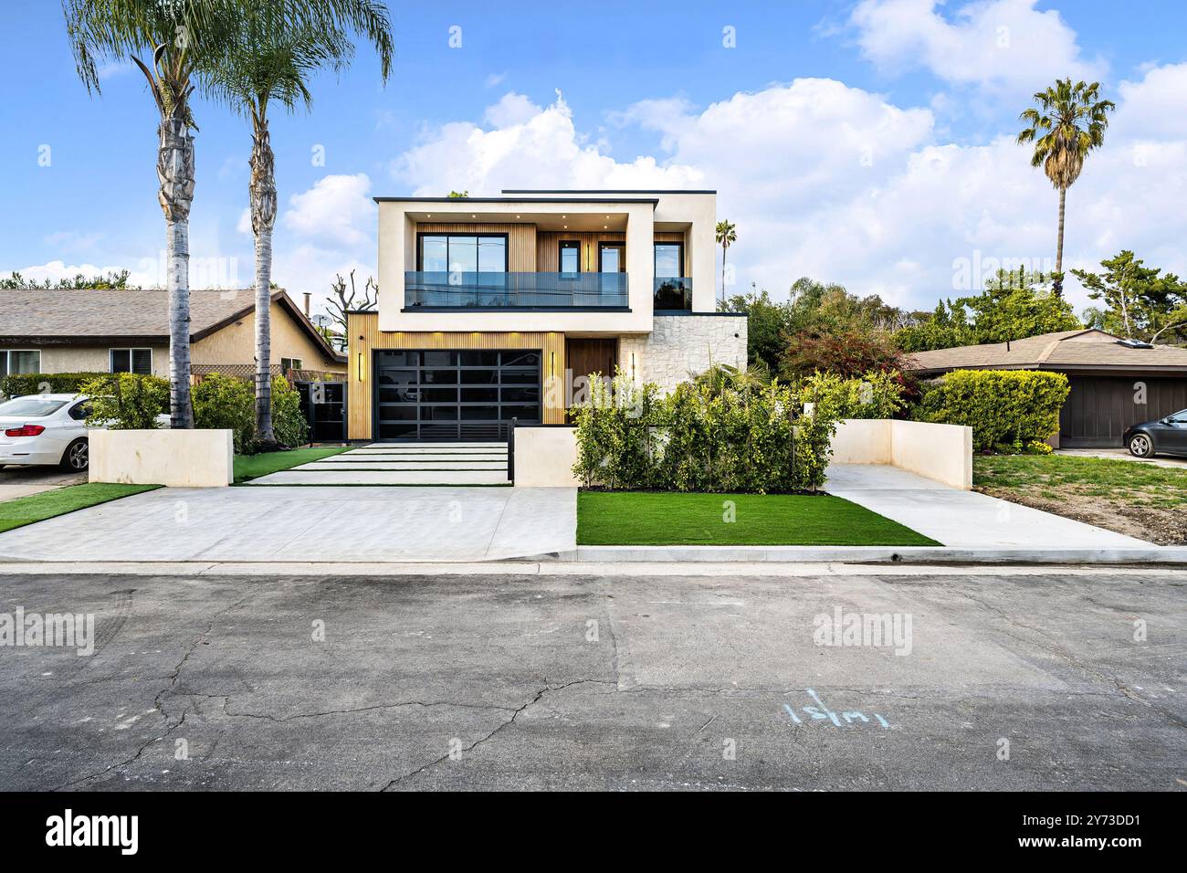 Moderna casa a due piani con grandi finestre, palme e un vialetto pulito sotto un cielo blu luminoso. Foto Stock