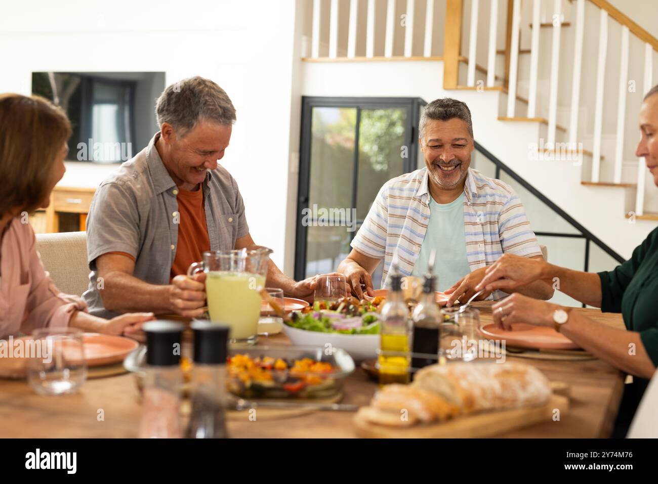 Pranza insieme, amici anziani e diversi che ridono e si gusta un pasto a tavola, a casa Foto Stock