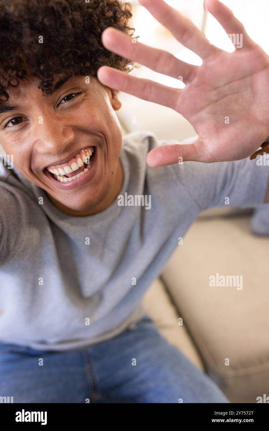 Un giovane sorridente che saluta e si diverte da solo a casa, in videochiamata Foto Stock