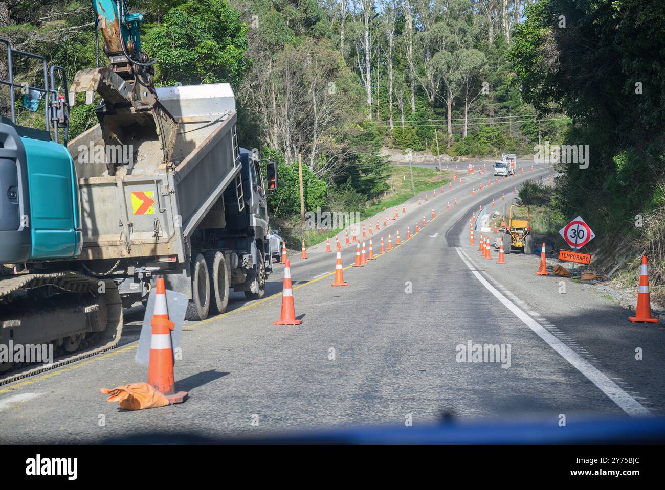 Digger al lavoro per strada. Il traffico arancione si snoda lungo l'autostrada. Lavori stradali alla baia di Hawke. Nuova Zelanda. Foto Stock