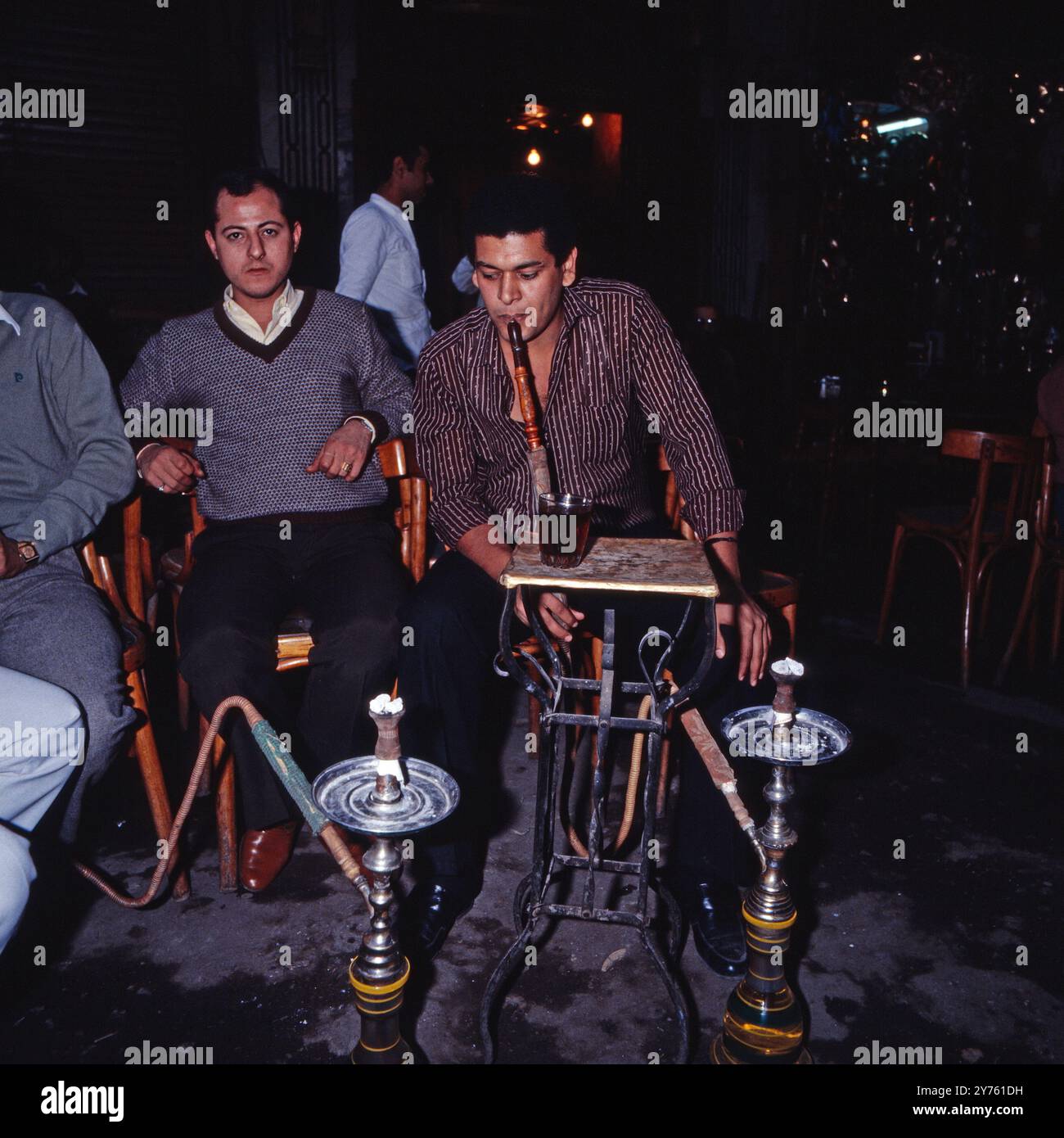 Männer sitzen im Kaffeehaus und rauchen eine Wasserpfeife im abendlichen Kairo, Ägypten um 1987. Foto Stock