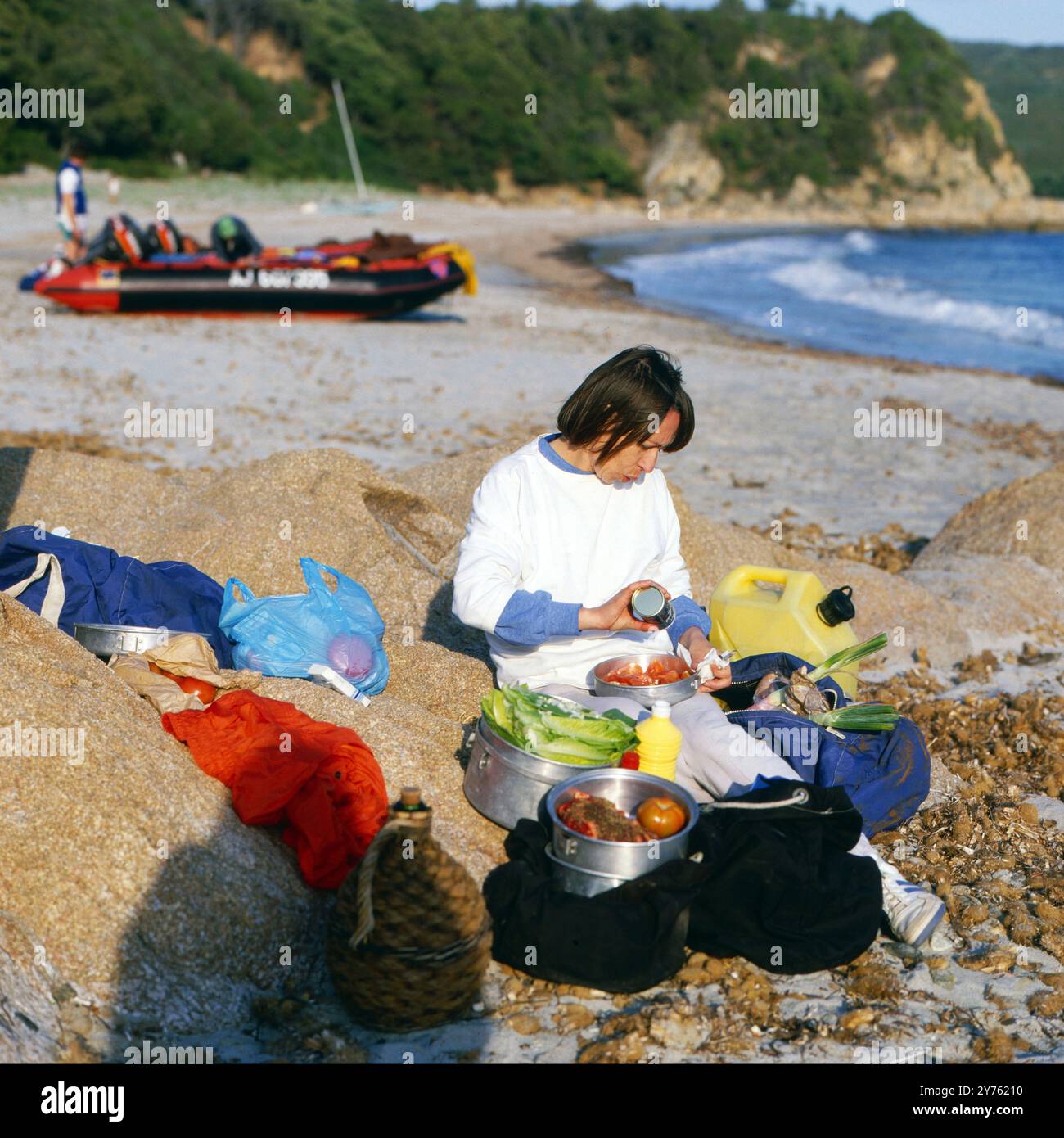 Teilnehmerin einer Schlauchbootrundfahrt kümmert sich am Strand um die Speisenzubereitung auf der Insel Korsika, um 1985. Foto Stock