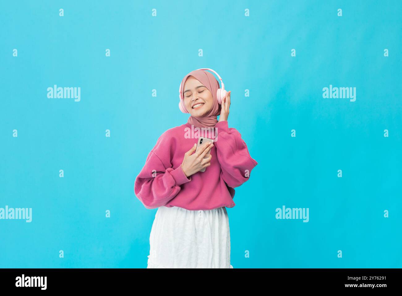Una giovane donna spensierata ama la musica con un elegante maglione rosa su un vivace sfondo blu Foto Stock