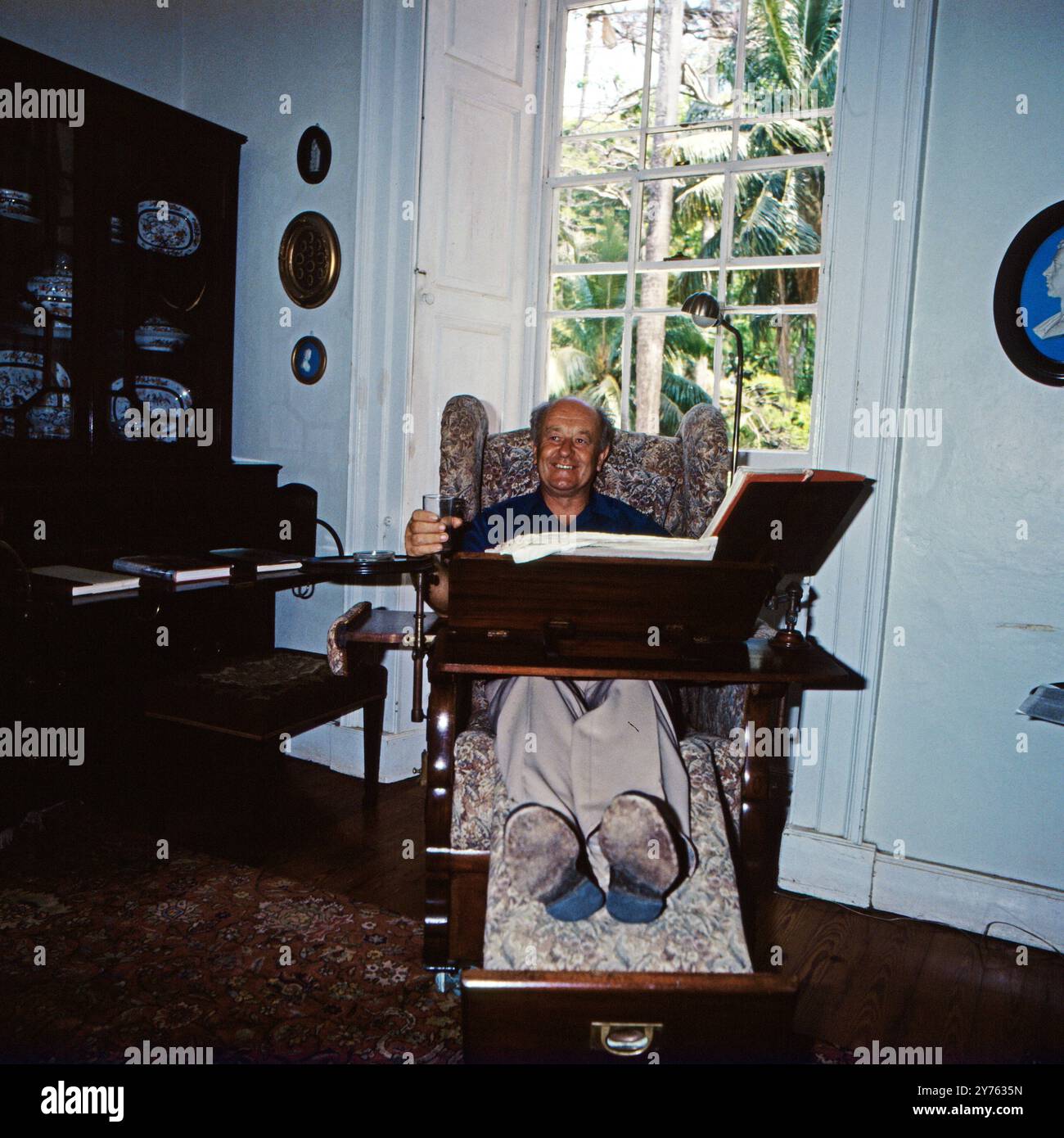 Ein Reisender Hat Platz genommen in einem hochinteressanten Multifunktionssessel mit Beinstüze, Arbeitstisch, Getränkehalter und Leselampe. Dieser befindet siich im Saint Nicholas Abbey Herrenhaus in Saint Peter auf Barbados, um 1985. Foto Stock