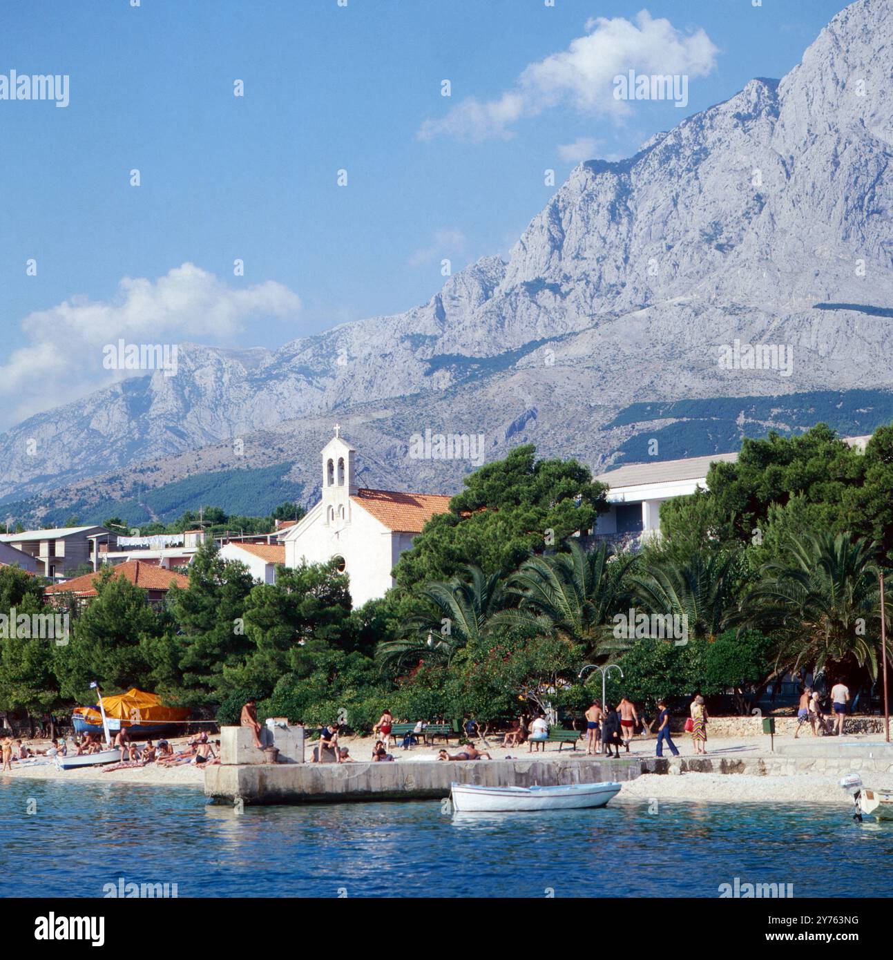 Hinter dem Strand von Baska Voda an der Makarska Riviera direkt die Stadt und die Kirche des Orts in der Region Kroatien, Jugoslawien um 1981. Foto Stock