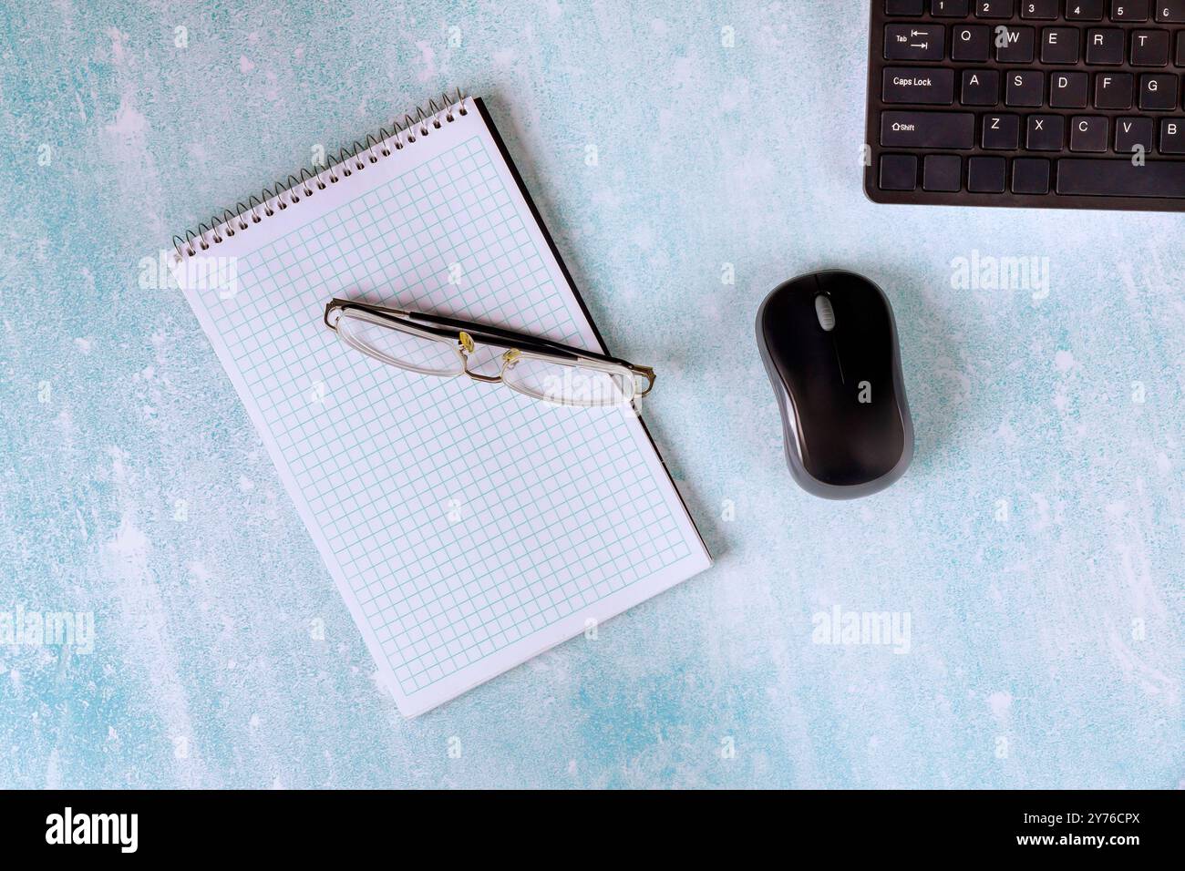 Il moderno tavolo da ufficio include notebook, occhiali, mouse e tastiera per lavorare. Foto Stock