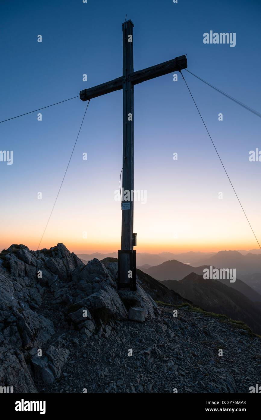 La croce sulla cima del monte Hinteres Sonnwendjoch contro la luce colorata dell'alba, Tirolo, Austria Foto Stock