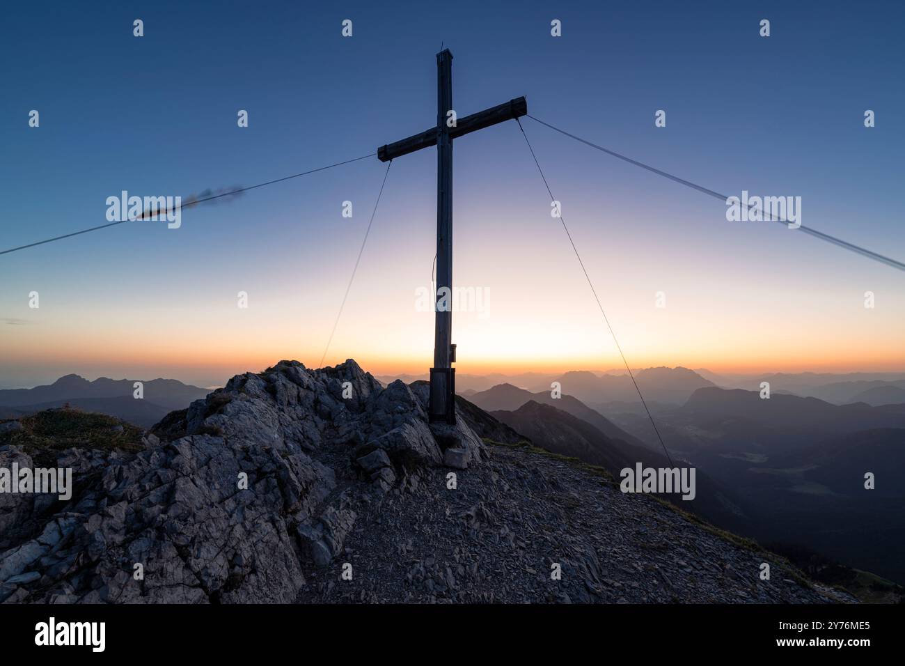 La croce sulla cima del monte Hinteres Sonnwendjoch contro la luce colorata dell'alba, Tirolo, Austria Foto Stock