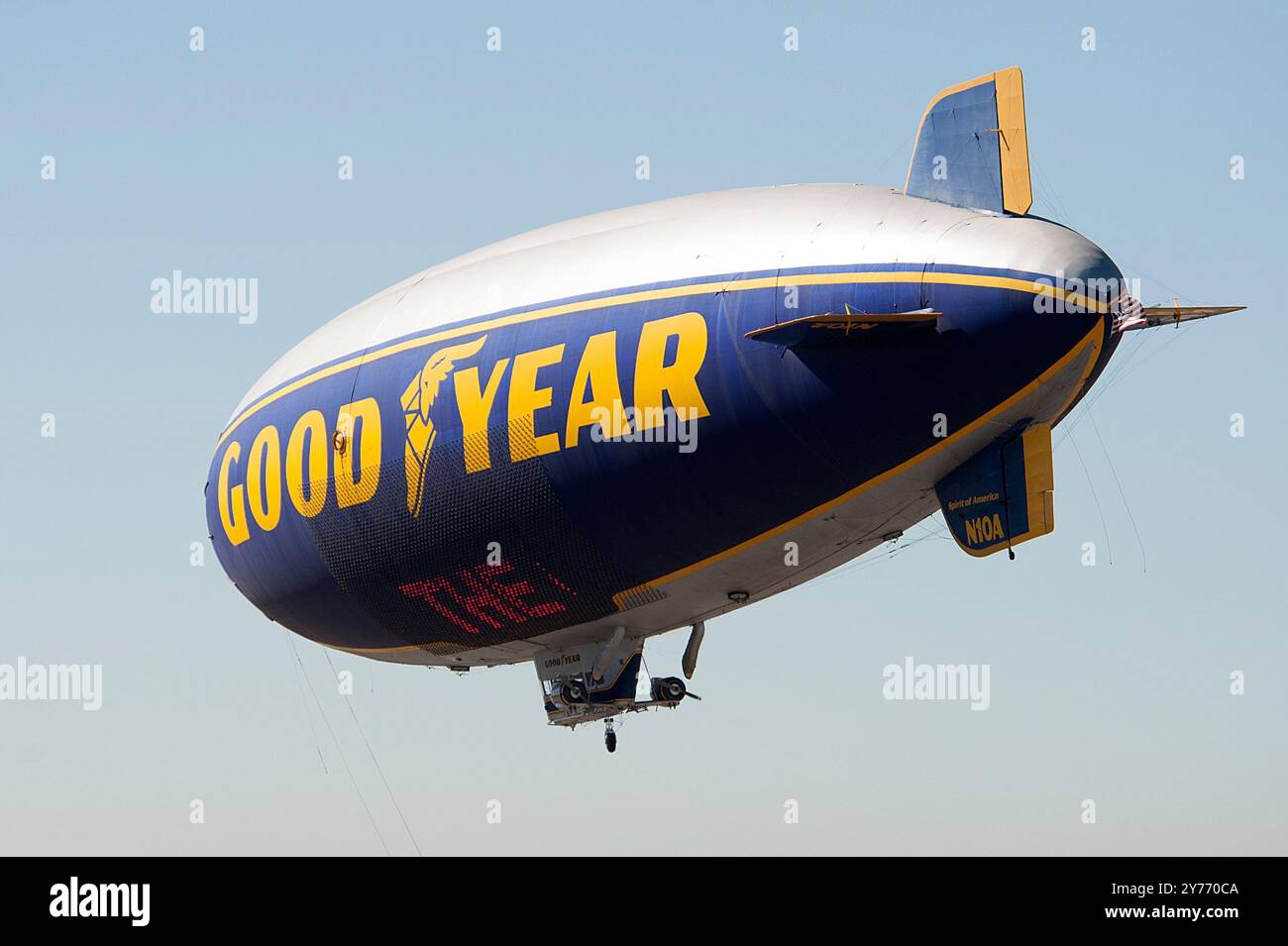 L'iconico Goodyear Blimp, simbolo dell'aviazione dirigibile, vola agevolmente sopra un aeroporto. Catturato contro un cielo limpido con vista degli hangar sottostanti Foto Stock