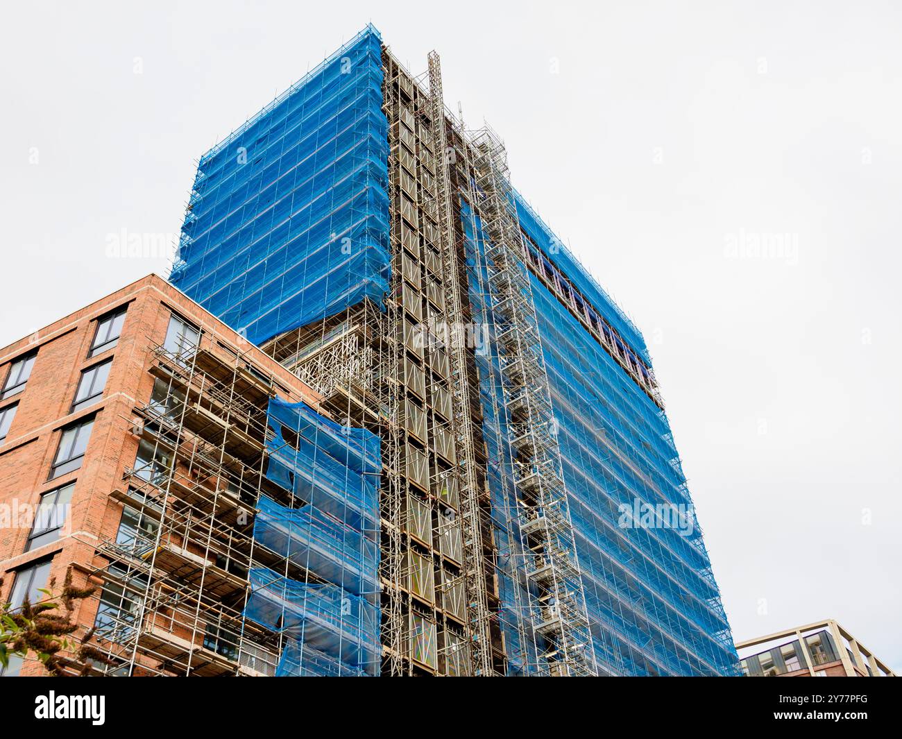 Un alto e moderno edificio in costruzione coperto da rete di sicurezza blu. Ponteggi circonda la struttura, mostrando il progresso dello sviluppo urbano Foto Stock