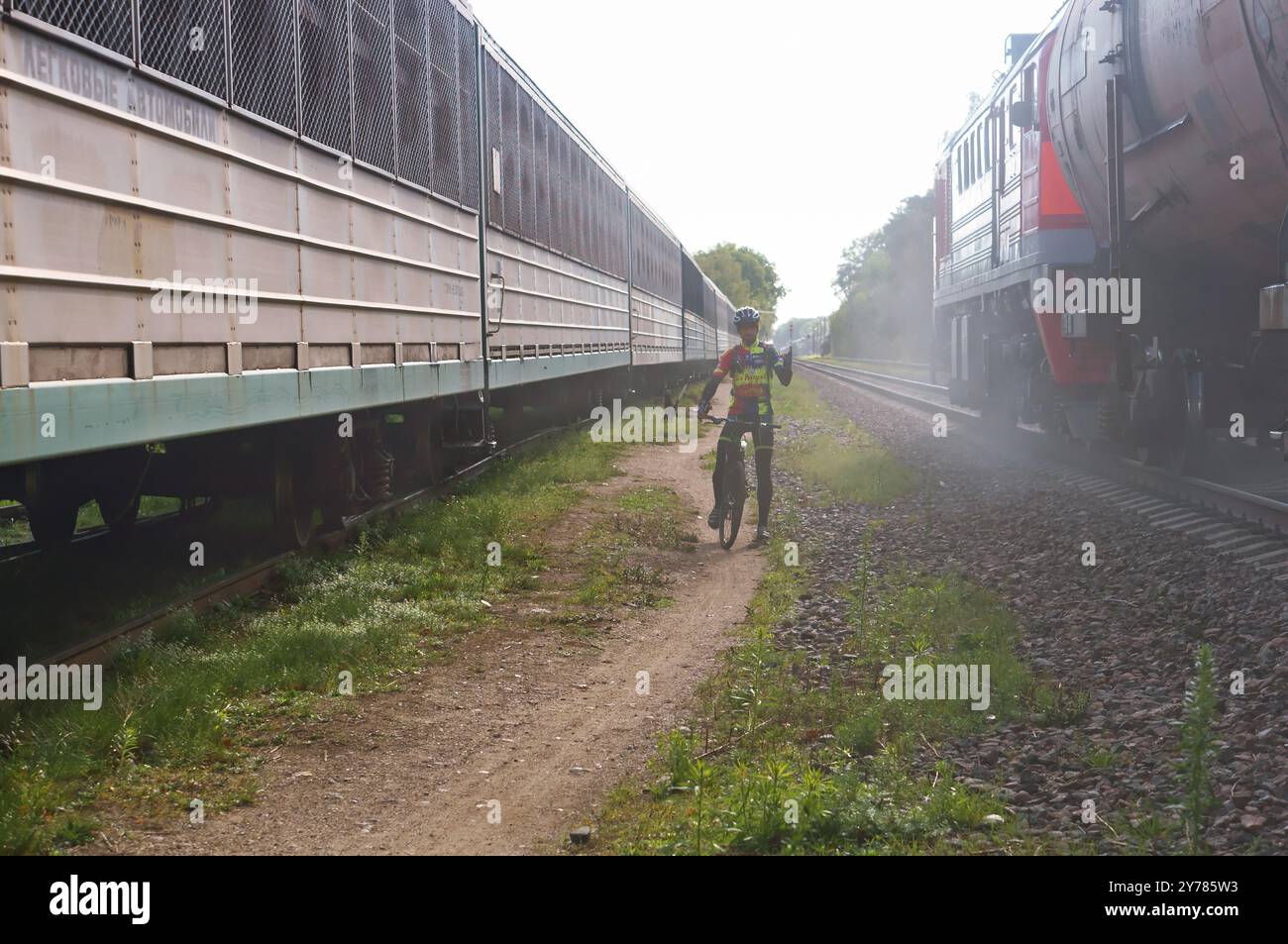 Ciclista tra due treni, ciclista su binari ferroviari, Kaliningrad, Russia 16 settembre 2018 Foto Stock