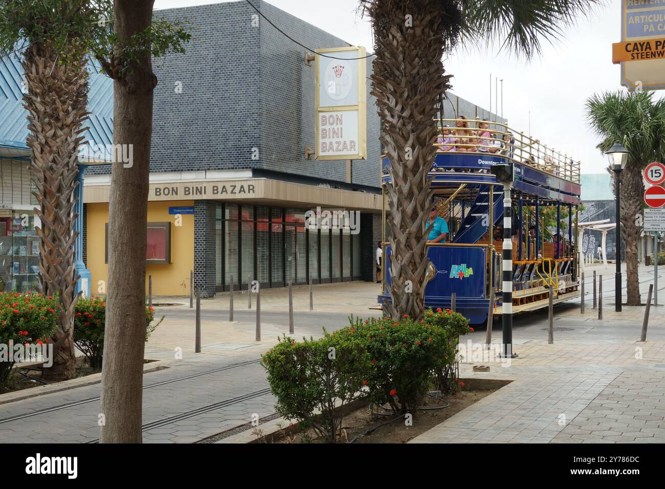 Tram blu del centro o tram pieni di turisti che passano per strade strette con edifici colorati e palme ad Aruba, a Oranjestad. Foto Stock