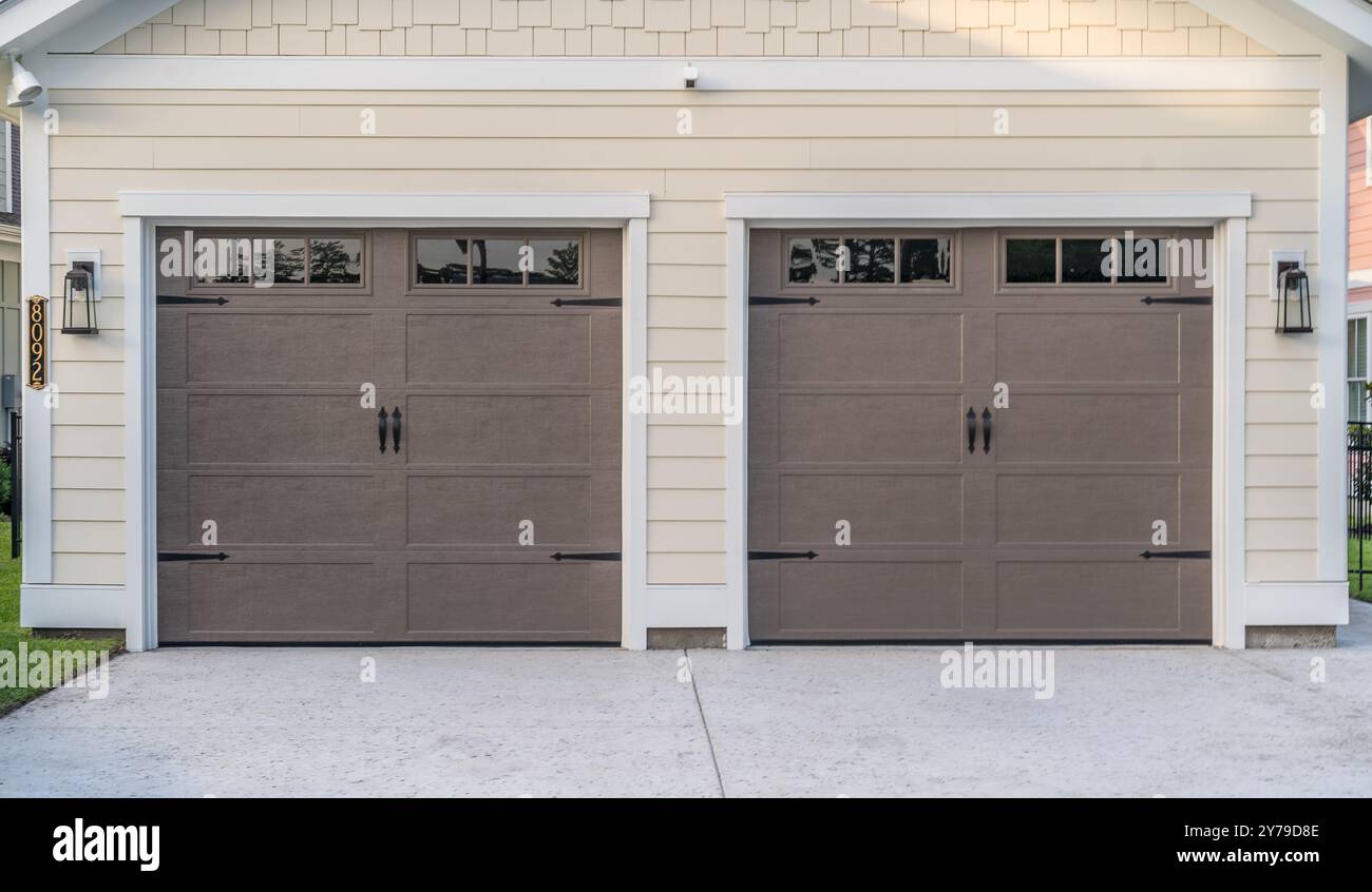 Porte elettroniche marroni per garage finestre luminose sullo specchio di poppa su un doppio vialetto di garage con fiancate orizzontali gialle in vinile, acciaio verniciato a polvere nero Foto Stock