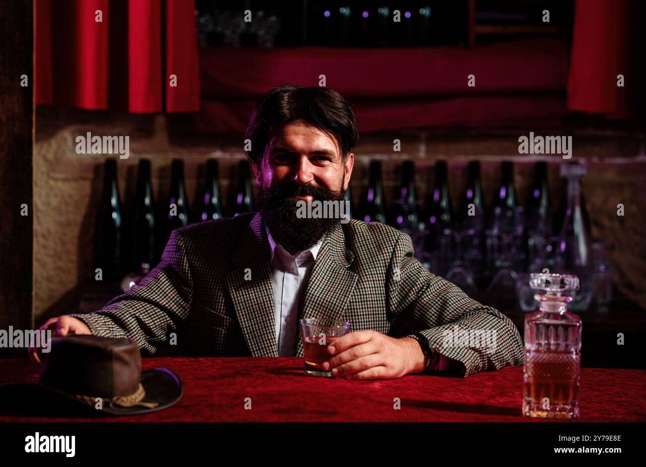 Uomo lavoratore vintage con barba lunga che tiene il whiskey. Seduto al bar. Foto Stock