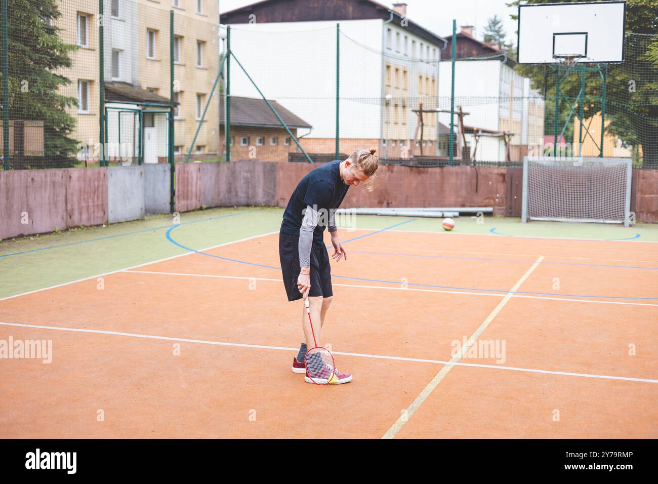 Il giocatore di badminton prende un rubinetto durante una partita su un campo all'aperto. Il momento informale si svolge in un ambiente urbano, con edifici circostanti Foto Stock Il giocatore di badminton prende un rubinetto durante una partita su un campo all'aperto. Il momento informale si svolge in un ambiente urbano, con edifici circostanti Foto Stock