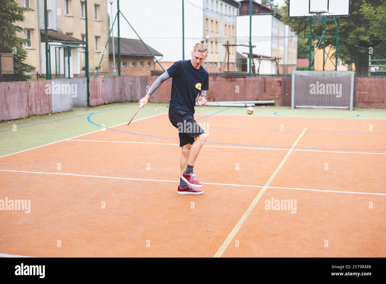 Il giocatore di badminton prende un rubinetto durante una partita su un campo all'aperto. Il momento informale si svolge in un ambiente urbano, con edifici circostanti Foto Stock Il giocatore di badminton prende un rubinetto durante una partita su un campo all'aperto. Il momento informale si svolge in un ambiente urbano, con edifici circostanti Foto Stock