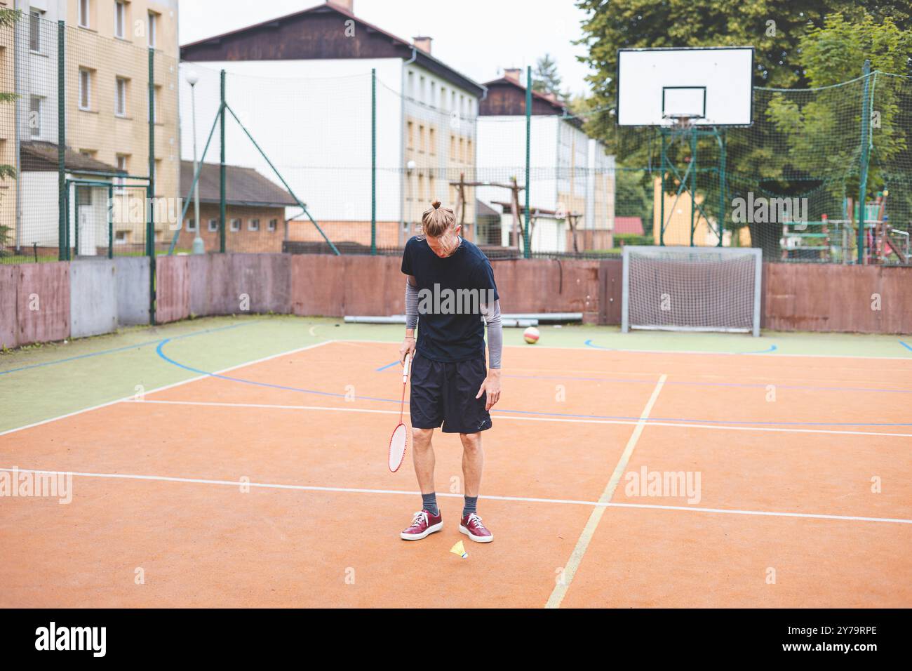 Il giocatore di badminton prende un rubinetto durante una partita su un campo all'aperto. Il momento informale si svolge in un ambiente urbano, con edifici circostanti Foto Stock Il giocatore di badminton prende un rubinetto durante una partita su un campo all'aperto. Il momento informale si svolge in un ambiente urbano, con edifici circostanti Foto Stock