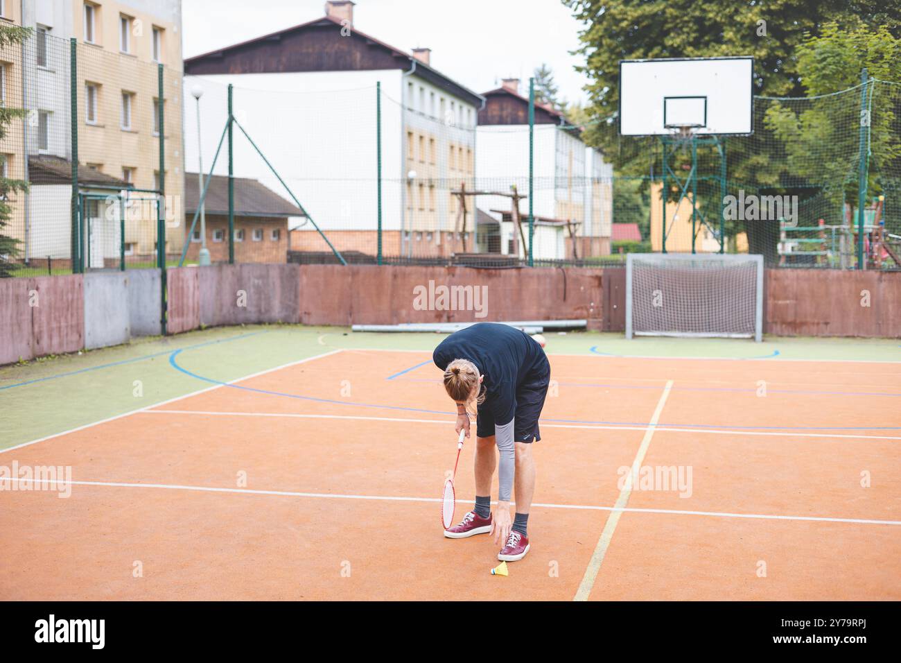 Il giocatore di badminton prende un rubinetto durante una partita su un campo all'aperto. Il momento informale si svolge in un ambiente urbano, con edifici circostanti Foto Stock Il giocatore di badminton prende un rubinetto durante una partita su un campo all'aperto. Il momento informale si svolge in un ambiente urbano, con edifici circostanti Foto Stock