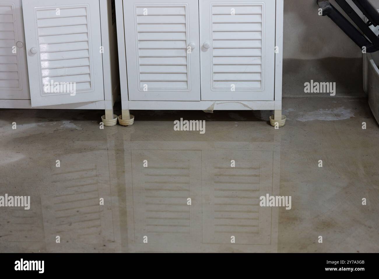 Spandimento dell'acqua. allagamento sul pavimento di cemento del magazzino in una casa che raggiunge le gambe degli armadi - danni agli effetti personali causati da perdite d'acqua Foto Stock