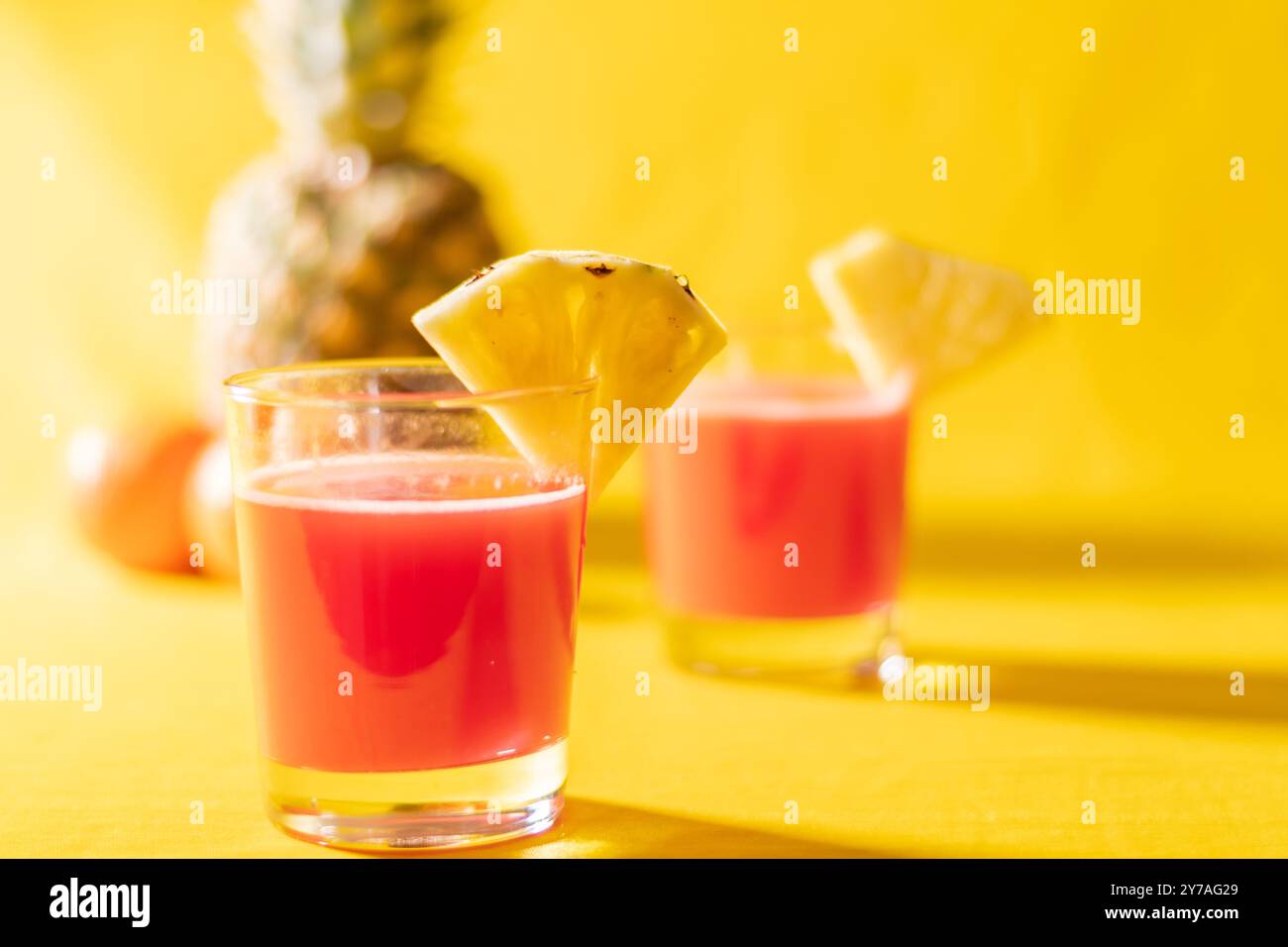 Succo di ananas in un primo piano di vetro vicino alla frutta tagliata a fette con spruzzi e liqid gocciolante per le vibrazioni estive. Sana bevanda biologica su sfondo arancione, c Foto Stock