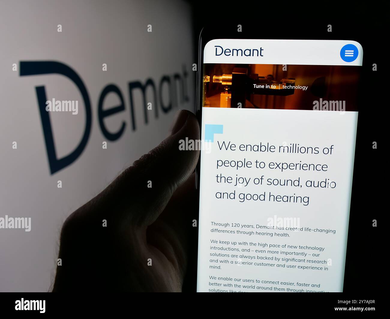 Persona che detiene un cellulare con pagina web della società danese di apparecchi acustici Demant COME sullo schermo di fronte al logo. Messa a fuoco al centro del display del telefono. Foto Stock