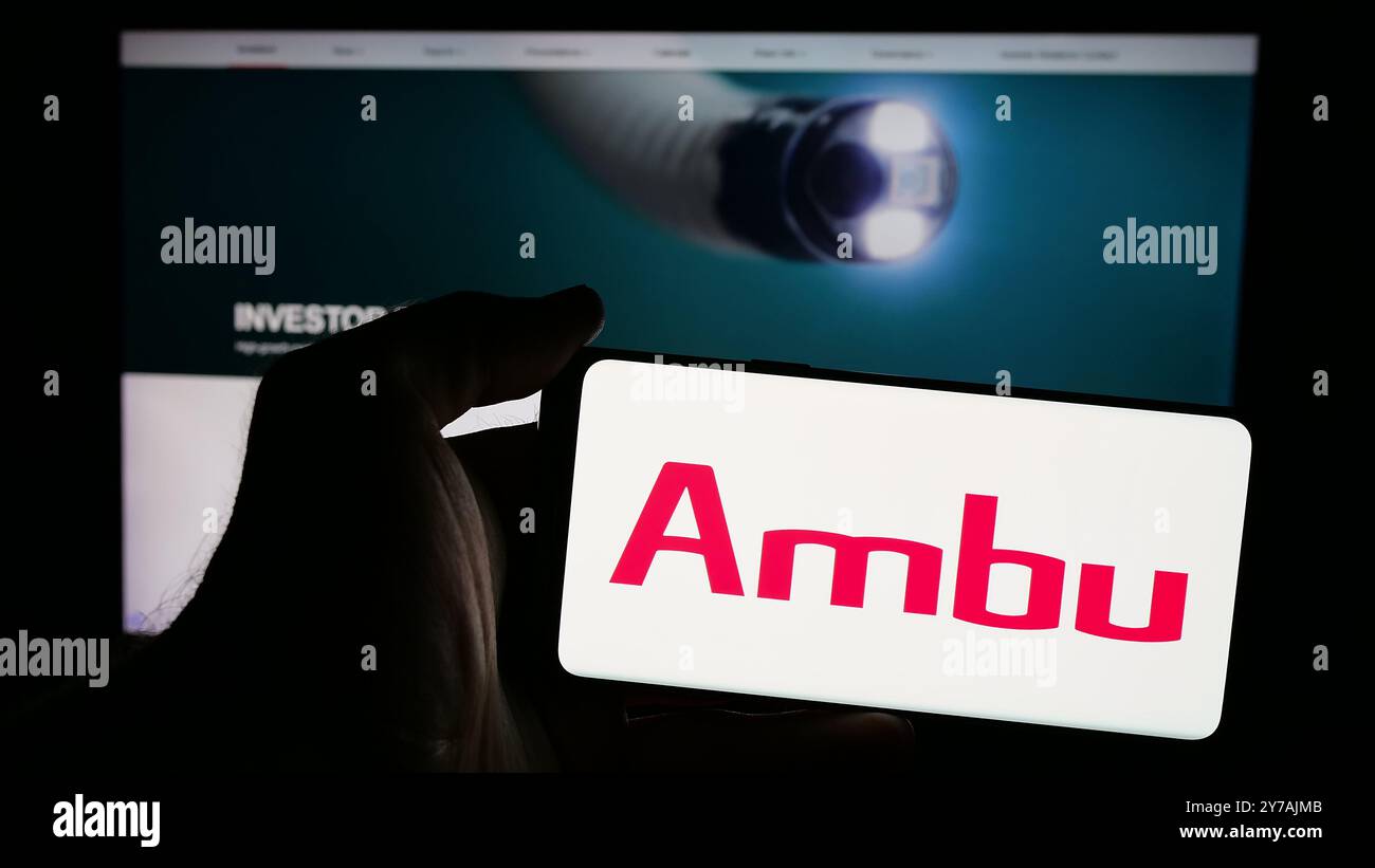 Persona che possiede uno smartphone con il logo della società danese di tecnologia medica Ambu sullo schermo di fronte al sito Web. Mettere a fuoco il display del telefono. Foto Stock