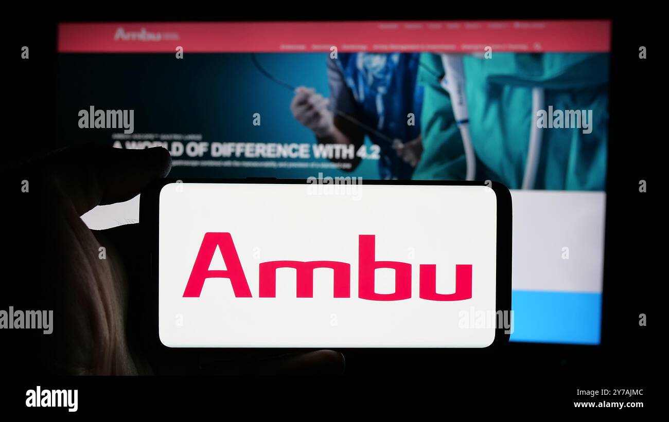 Persona che detiene il cellulare con il logo della società danese di tecnologia medica Ambu COME sullo schermo di fronte alla pagina web aziendale. Mettere a fuoco il display del telefono. Foto Stock