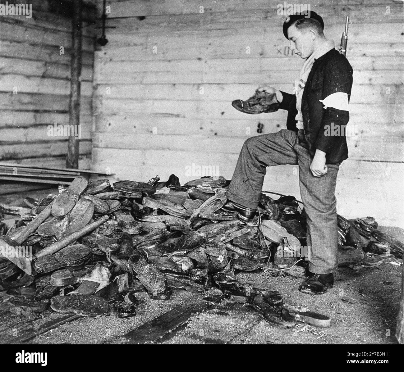 Un giovane membro della resistenza francese esamina stivali, scarpe e zoccoli di legno accumulati vicino a una fornace nel crematorio del campo di concentramento di Natzweiler-Struthof. Questo campo, in Alsazia, era l'unico campo nazista sul suolo francese. Era un campo di lavoro, un campo di transito e, con l'avanzare della guerra, un luogo di esecuzione. Si stima che 22.000 persone siano morte lì. Foto Stock