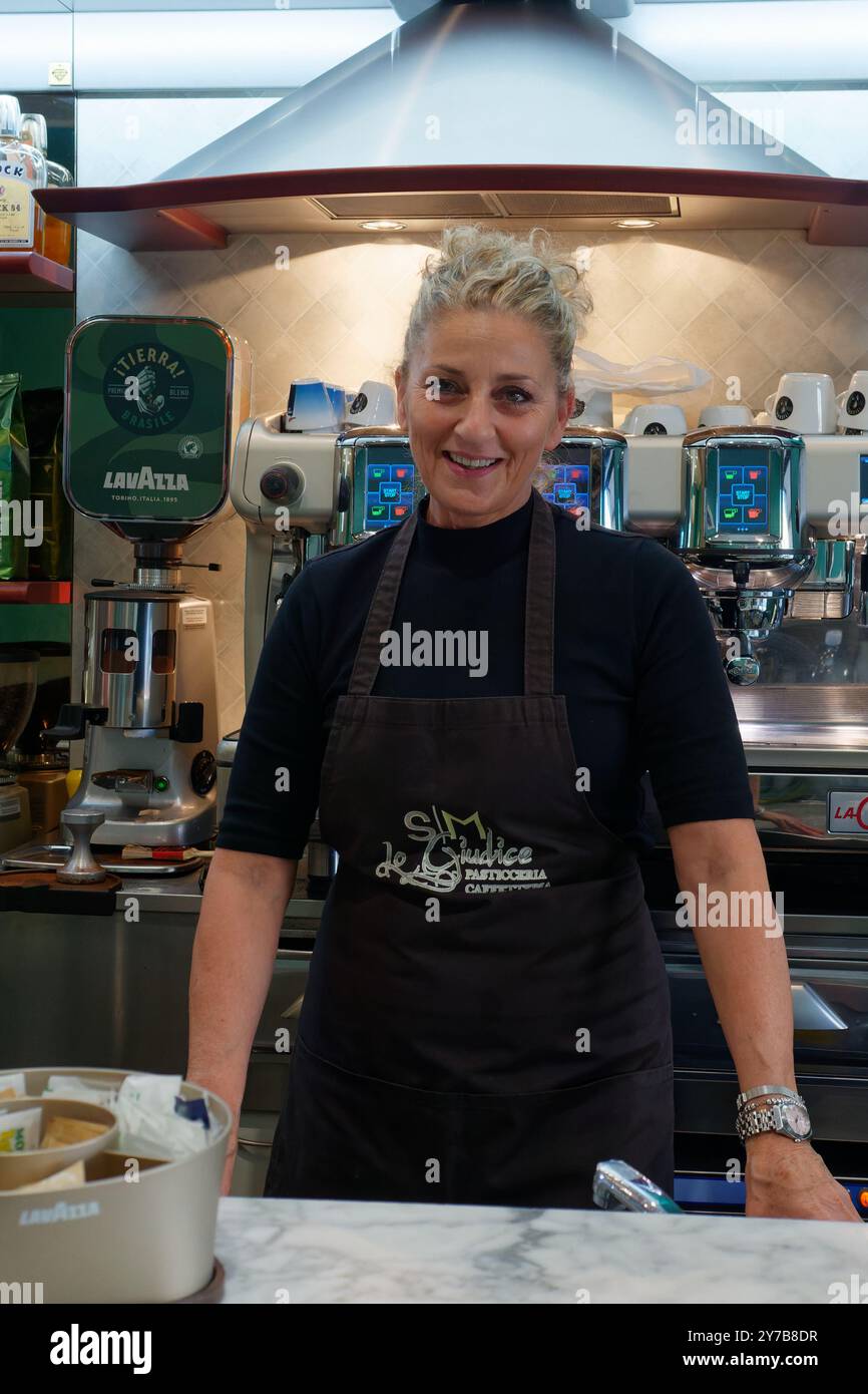 Barista donna che indossa un grembiule e sorride in una caffetteria (Bar/pasticceria) nella città di Montefiascone, Lazio, Italia. Settembre 28/29 2024 Foto Stock