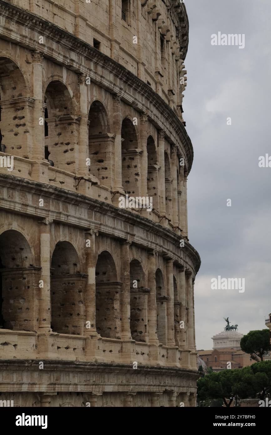 L'antico e iconico Colosseo di Roma (Anfiteatro Flavio) con le sue centinaia di archi e la facciata in travertino decorata, adiacente al foro Romano Foto Stock