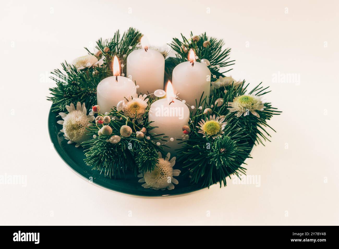quattro candele bianche dell'avvento, decorazioni a corona con fiori e pini, isolate, quattro candele dell'avvento accese Foto Stock