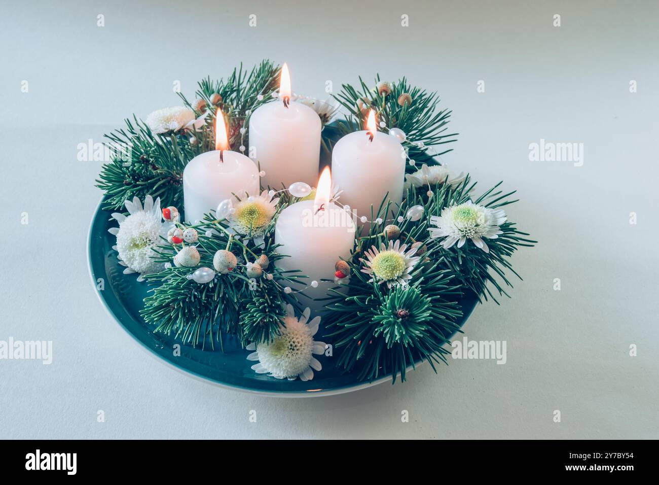 quattro candele bianche dell'avvento, decorazioni a corona con fiori e pini, isolate, quattro candele dell'avvento accese Foto Stock