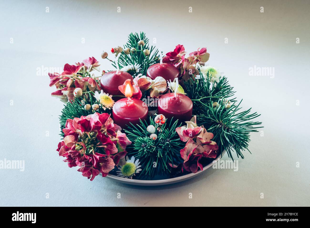 quattro candele bianche dell'avvento, decorazioni a corona con fiori e pini, isolate, una candela dell'avvento bruciata Foto Stock
