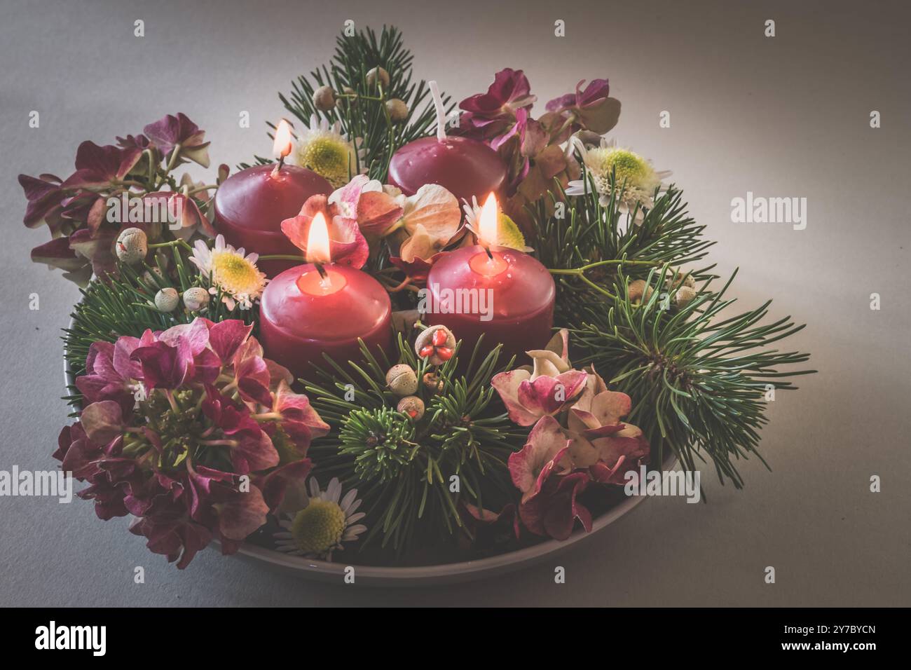 quattro candele bianche dell'avvento, decorazioni a corona con fiori e pini, isolate, tre candele dell'avvento in fiamme Foto Stock