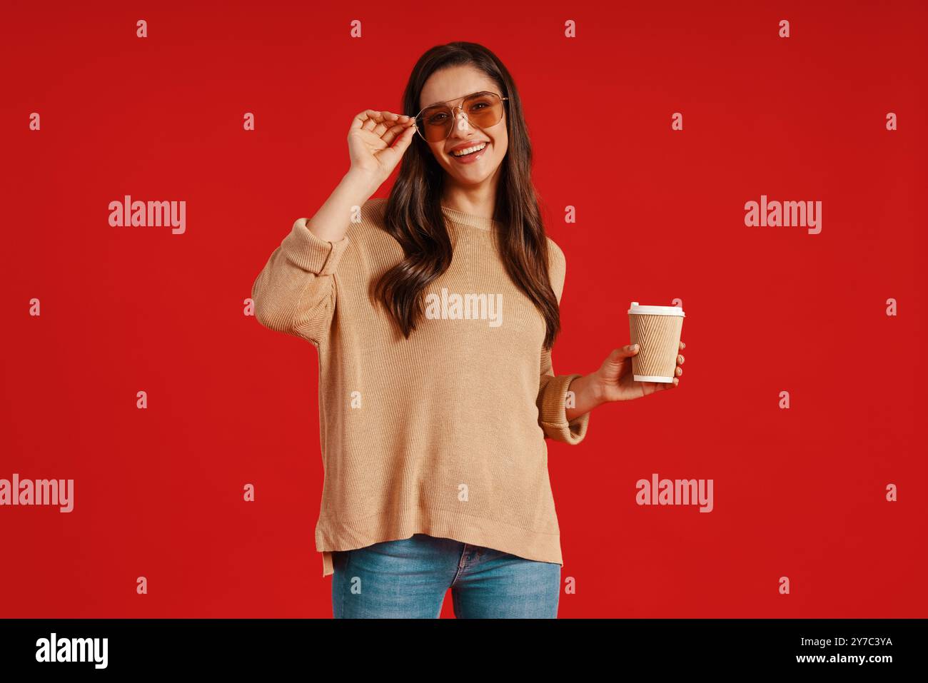 Bella giovane donna in abbigliamento casual che sorride e regola gli occhiali stando in piedi su sfondo rosso Foto Stock