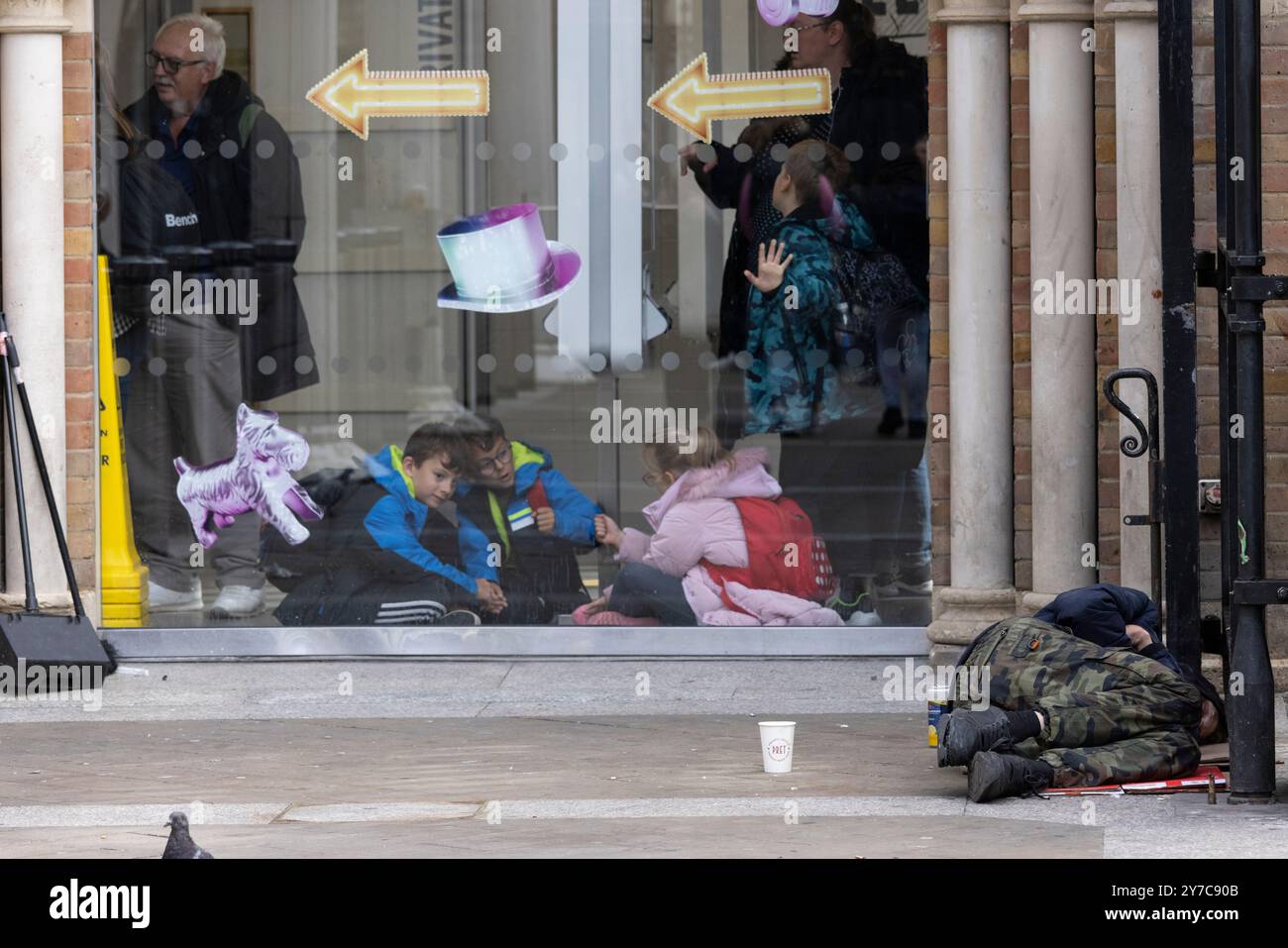 I tossicodipendenti senzatetto giacciono a terra mentre i pedoni fanno la loro vita quotidiana fuori dall'ingresso della stazione di Liverpool Street, City of London, Regno Unito Foto Stock