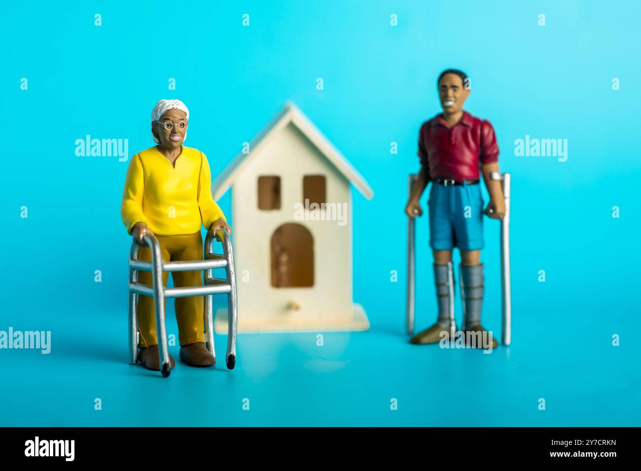 Diversi anziani con ausili per la mobilità in piedi modello di casa su sfondo blu. Foto Stock