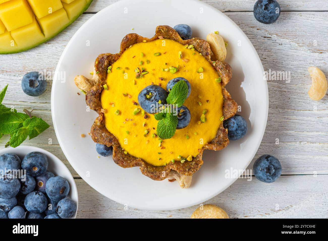 Torta di mango gialla vegan cruda con mirtilli freschi, pistacchi e menta. Crostata sana e deliziosa senza glutine. Dessert Vegan cheescake. Vista dall'alto Foto Stock