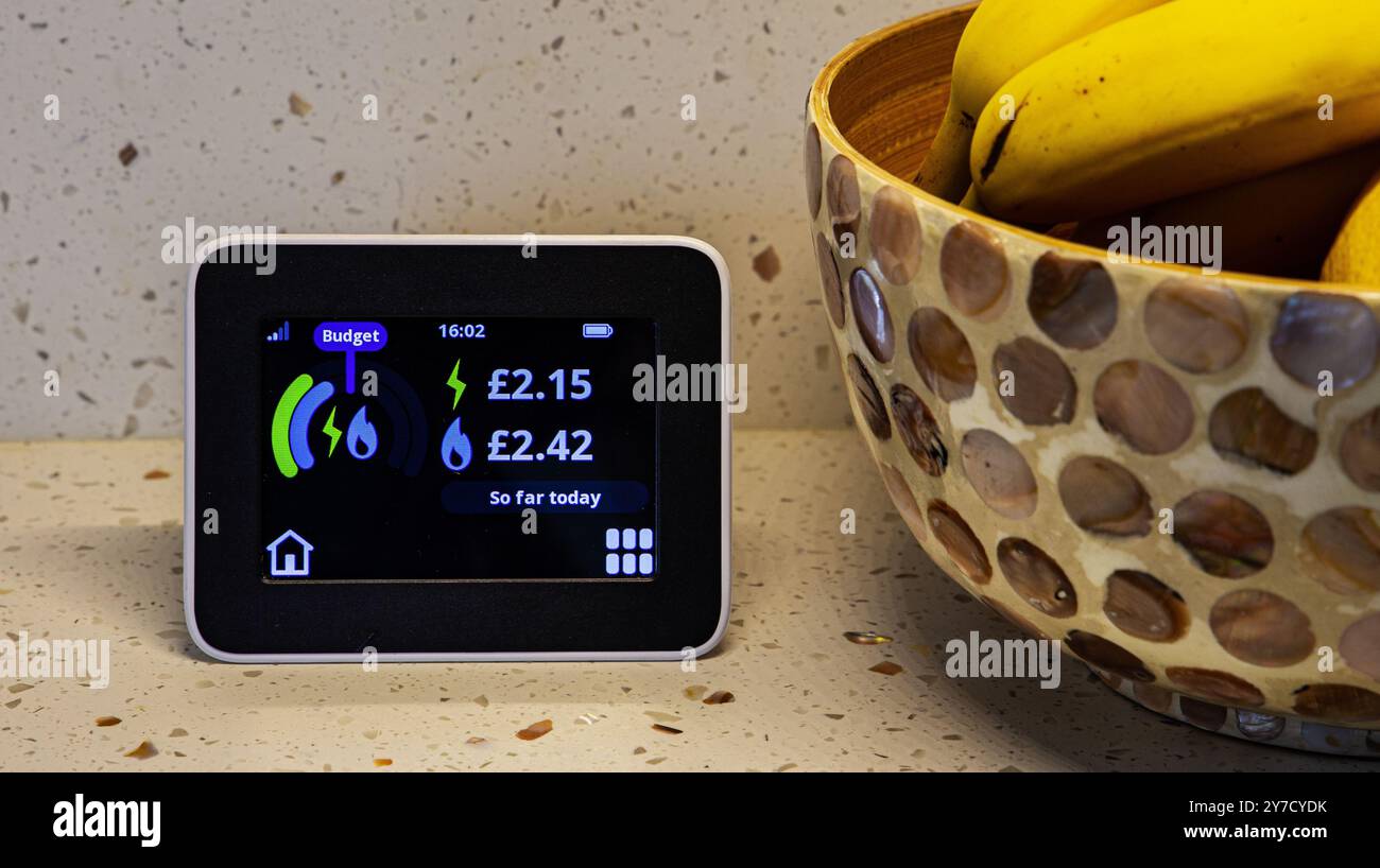 Contatore intelligente dell'energia domestica che mostra l'uso di elettricità e gas con una ciotola di banane su un piano di lavoro della cucina Foto Stock