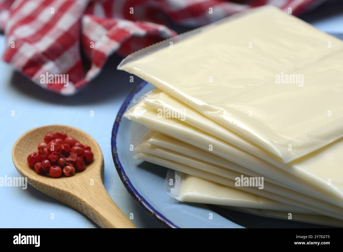 Formaggio lavorato, fette di formaggio lavorato avvolte in plastica e cucchiaio di bacche rosa, pepe rosso Foto Stock