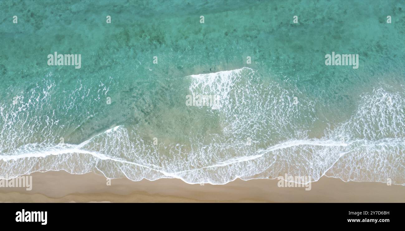 Le onde dell'oceano baciano la spiaggia sabbiosa sullo sfondo di una spiaggia tranquilla Foto Stock