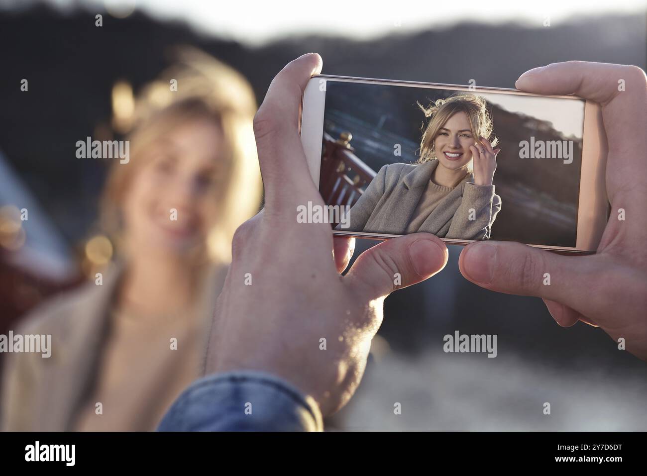 Un uomo realizza un ritratto al telefono di una donna sorridente sul ponte nelle soleggiate giornate primaverili o autunnali all'aperto Foto Stock