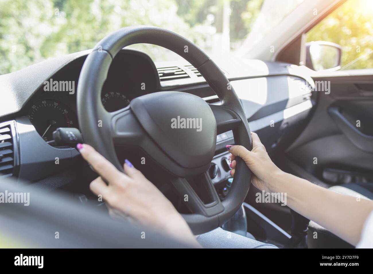 Ravvicinato le mani della donna che tengono il volante mentre si siede nell'abitacolo moderno del veicolo. Ragazza che guida l'auto al concetto di strada Foto Stock