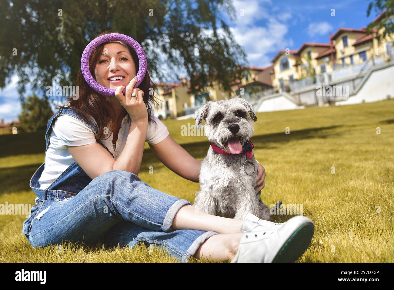 Caucasian donna allegra giocando con il suo amato cane nel parco. Il concetto di amore per gli animali. migliori amici. Cane di razza Schnauzer Foto Stock