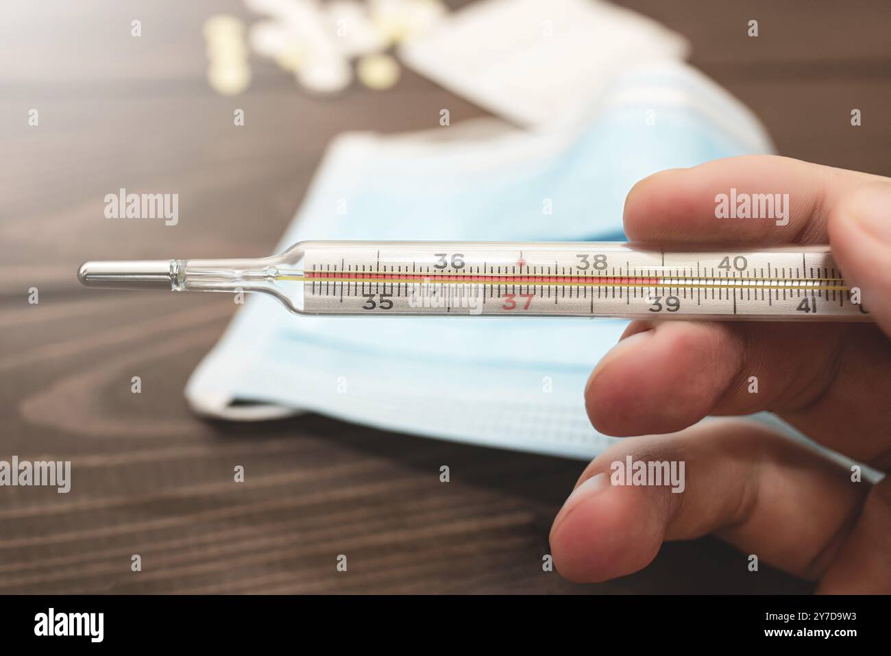 Termometro medico-clinico a mercurio in mano che mostra la temperatura di 39 C. alta temperatura. Fondo in legno. Tema della sanità, io Foto Stock