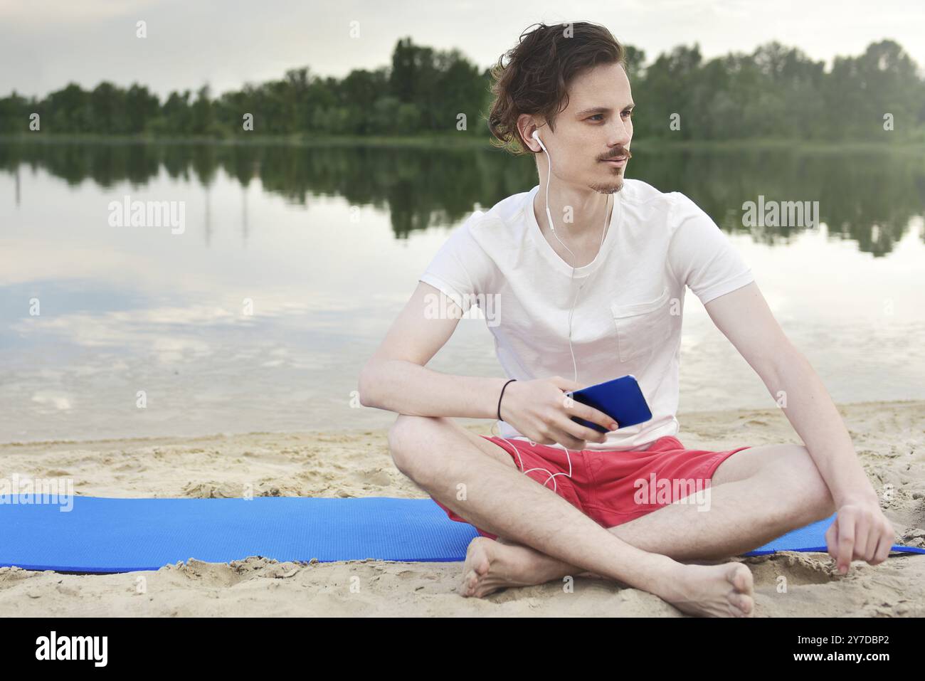 Giovane uomo a camminare vicino alla bellissima baia usando il telefono e cuffie per comunicare con amici e ascolto di musica Foto Stock