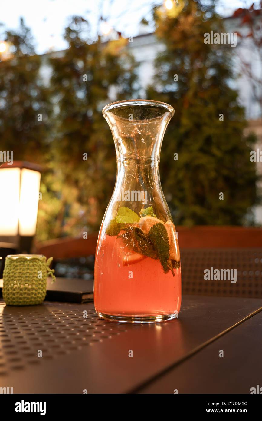 Una tranquilla serata all'aperto con una caraffa di vetro ripiena di limonata e guarnita con menta e limone. Un'illuminazione calda e una luce soffusa creano Foto Stock